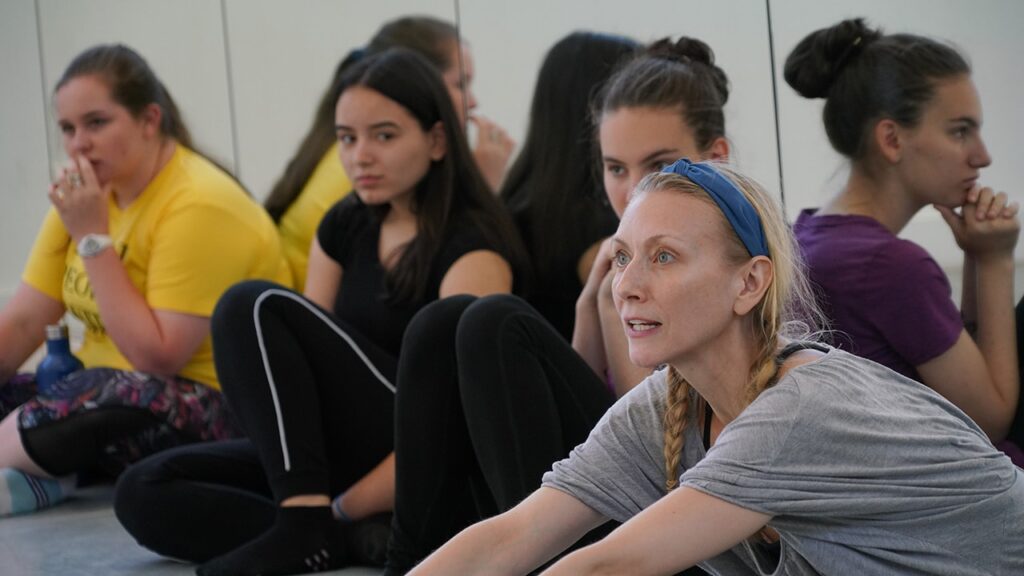 Four woman sit on the floor with a mirror behind them looking out.