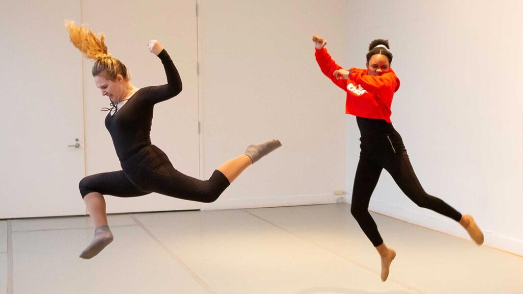 Two woman dance jumping in the air. Anger in their faces and hands in fists.